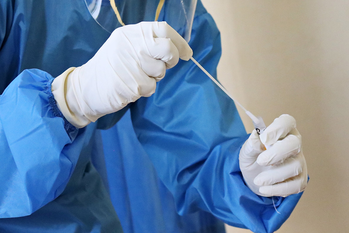 Health care worker in blue scrubs putting a swab in a test tube.