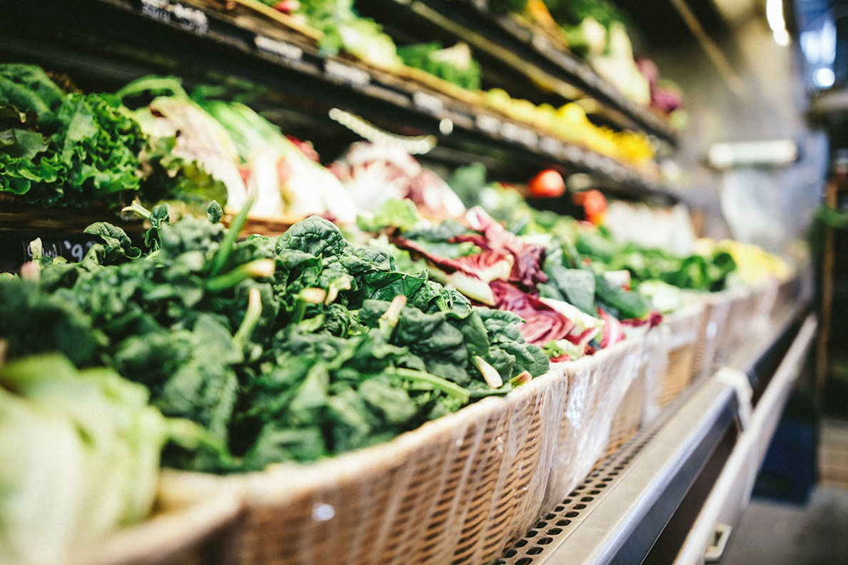 A produce aisle in a grocery store featuring spinach greens and other vegetables.
