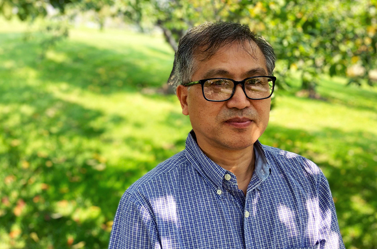 Closeup of Frank Zhao in a grassy area with trees.