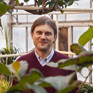 Andrei Smertenko standing in a greenhouse with plants around him.