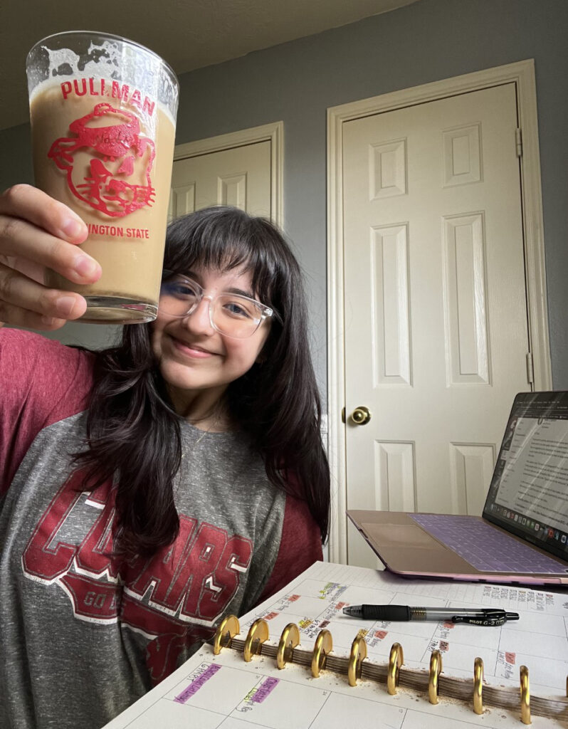 A WSU Global Campus student holding a Cougar-themed drinking glass next to a laptop and notebook.