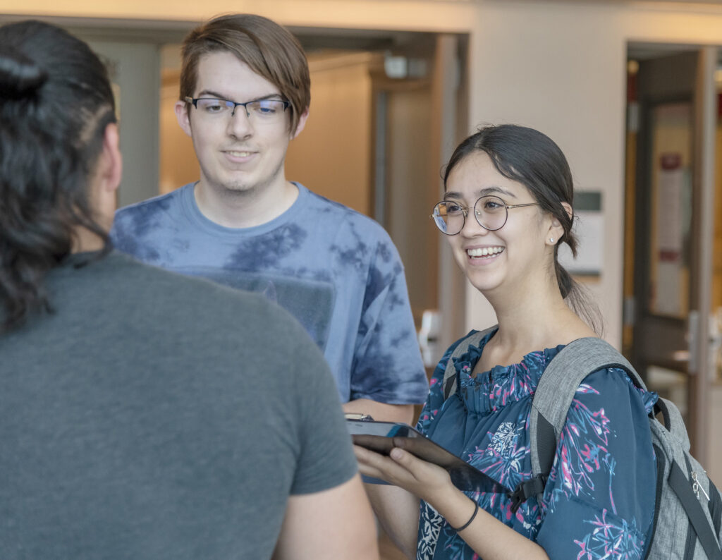 A student holding a clipboard and talking to other students.