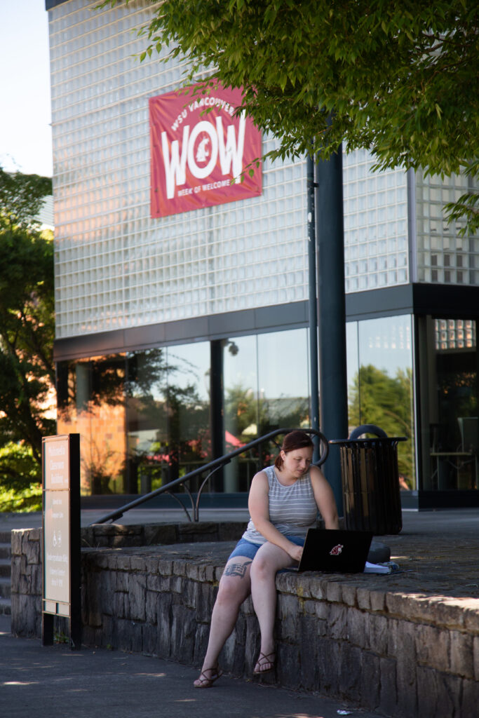 Student using a laptop outside a building on the WSU Vancouver campus.