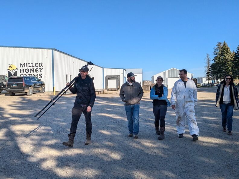People walking on gravel road, one holding a camera and tripod