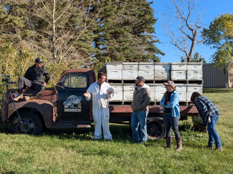 Group of collaborators standing by truck with honey bee hives on bed of truck