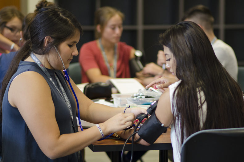 A counselor shows a teenage participant in Na-ha-shnee Native American Health Sciences Institute how to measure blood pressure.