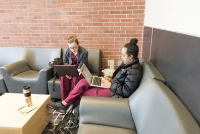 Two students in scrubs sit looking at their laptops.