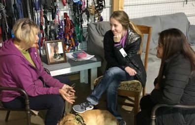 Two students talk to an older woman, with a dog laying on the ground between them.