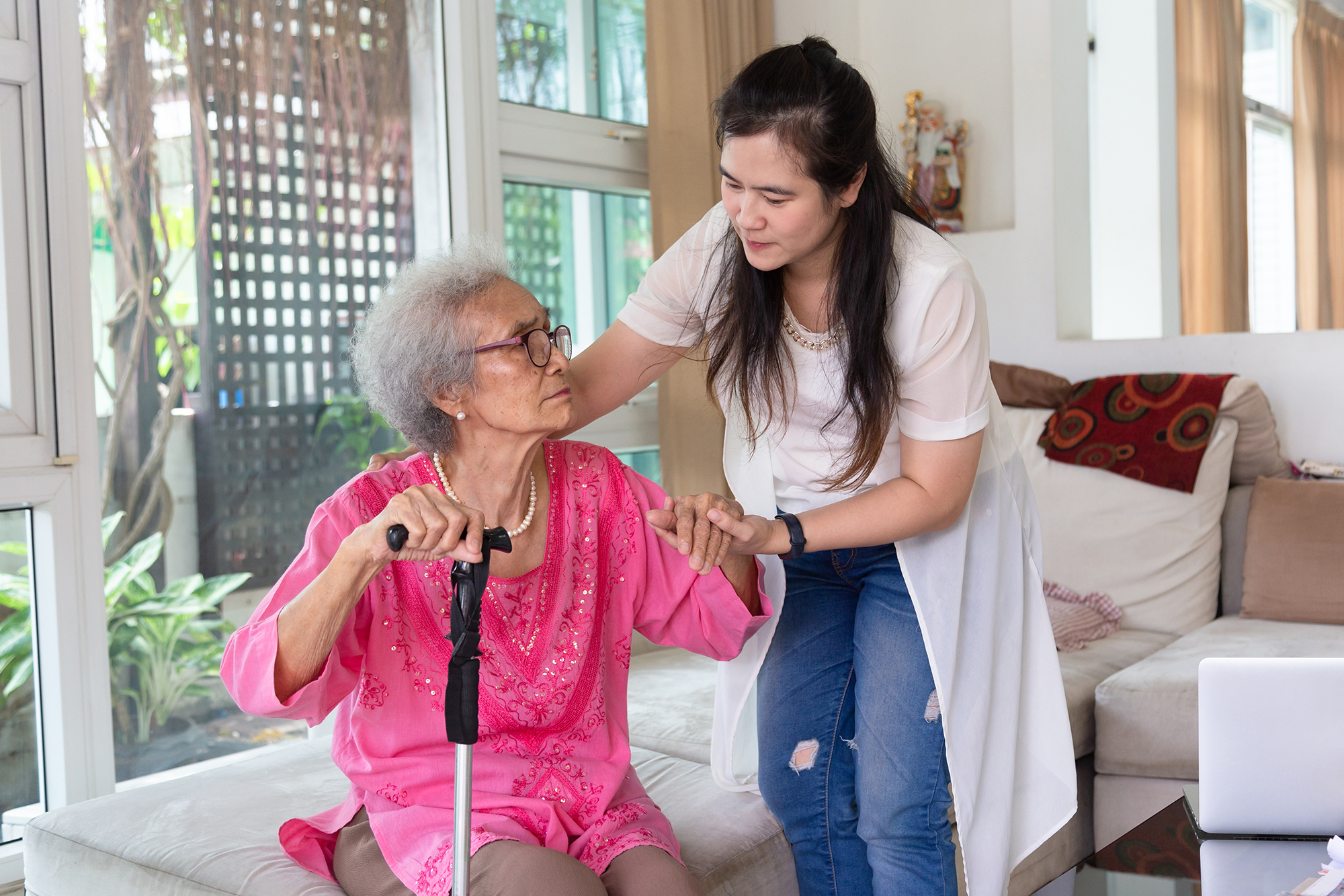 Young carer supporting senior disabled woman with walking stick