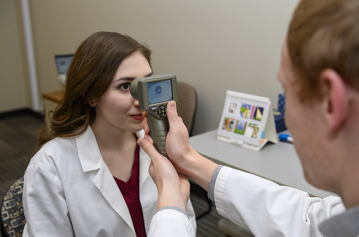A staff member in Georgina Lynch’s lab demonstrates the use of a handheld monocular pupillometer to measure the pupillary light reflex.