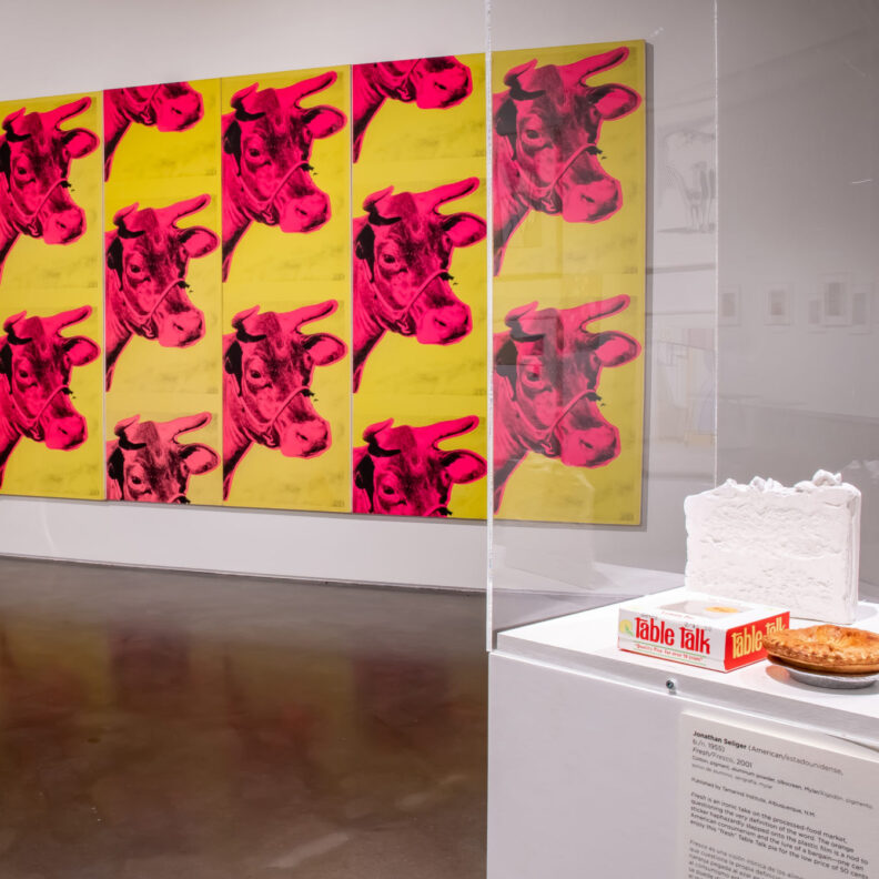 A gallery with art on a wall showing a pink cow on a yellow background.