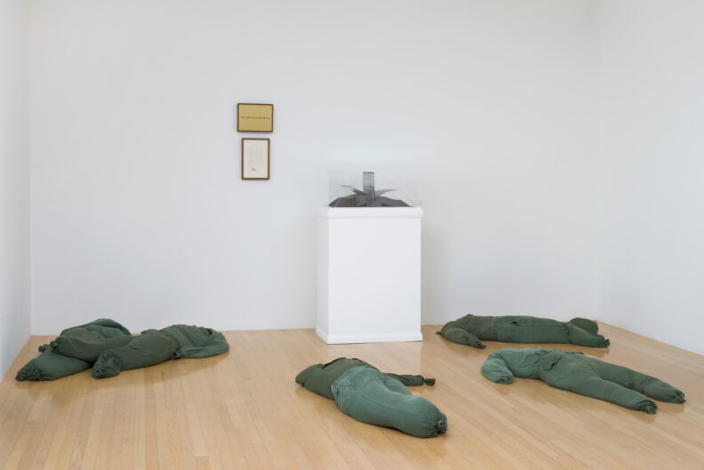 Stuffed clothing laying on a gallery floor with a display of an open book.