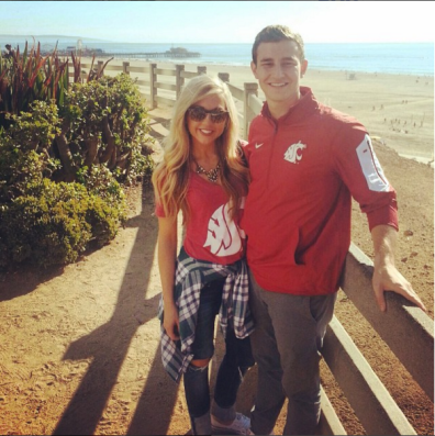 Two WSU Cougs dressed in WSU Coug gear in front of a guardrail at the beach.