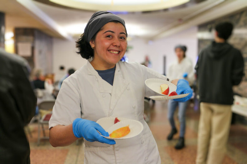 A graduate student holds up plates of apple slices.