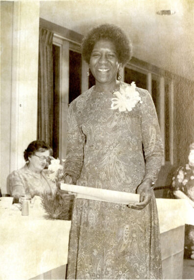 Black and white picture of Gladys Jennings. She smiles and holds a piece of paper.