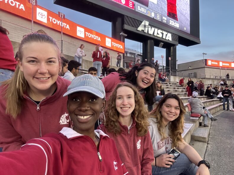 Katie and her lab group are seated together during a WSU football game. They all wear WSU merch.
