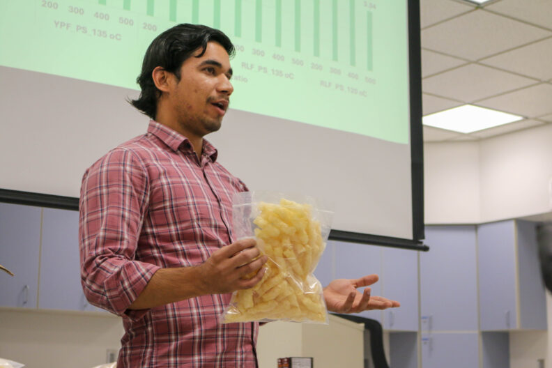 A graduate student holds up a bag full of extruded pieces.