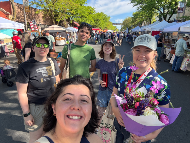 A group of people stand in the middle of a street closed off for pedestrians. One person of the group holds up a beautiful bouquet. 
