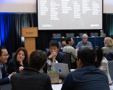People are seated together at tables, talking with each other.