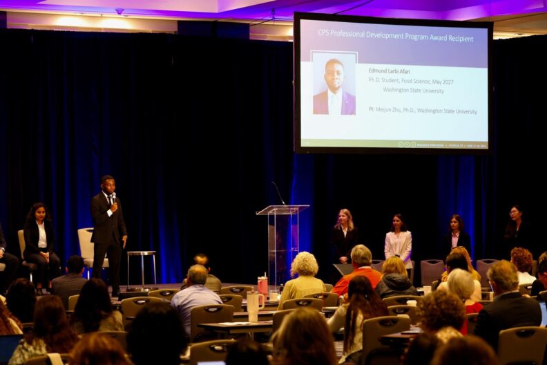 Edmund stands on a stage, speaking to a crowd.