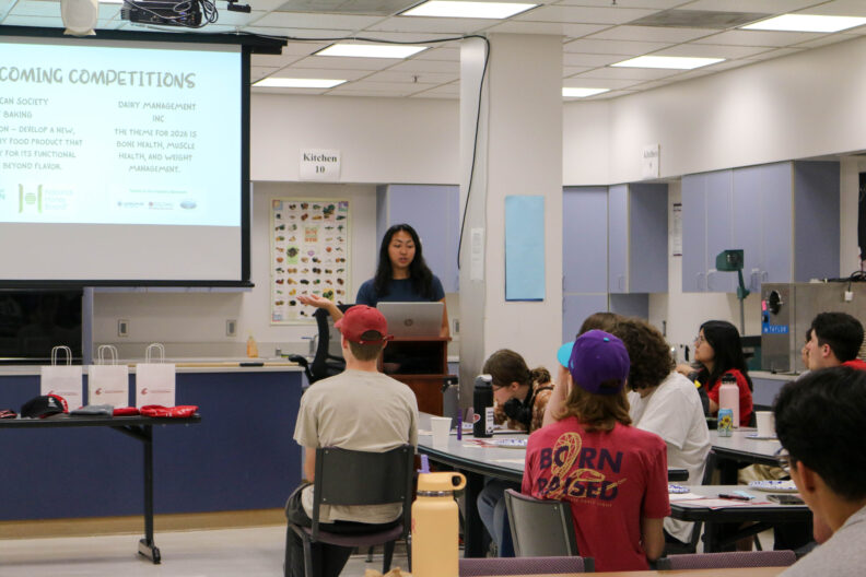Natalie speaks at a podium. A group of students are seated, listening.