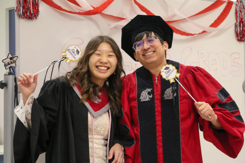 Two students, Christine and Alejandro, stand together and hold up wands that say "class dismissed."