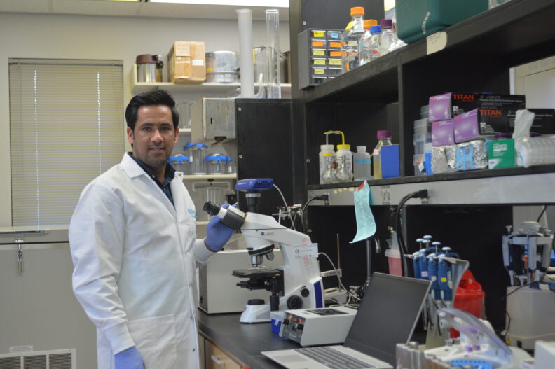 Barakatullah in a lab. He has one hand on a microscope.