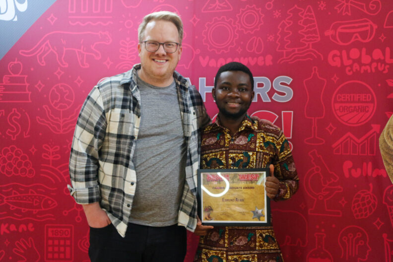 Edmund stands beside the person who nominated him, holding his award.