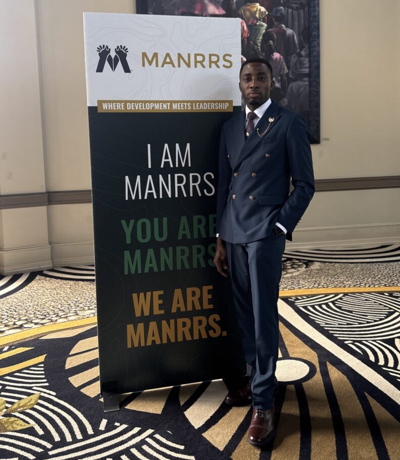 Paul poses next to a sign that says, "I am MANRRS, you are MANRRS, we are MANRRS."