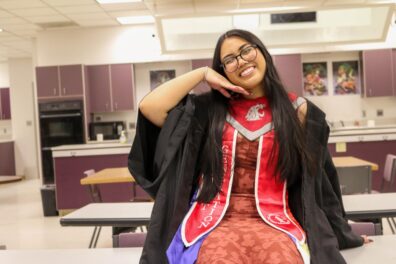 Sherine in grad attire, sitting on top of a table and posing.