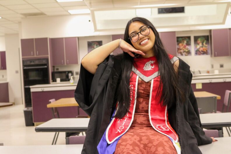 Sherine in grad attire, sitting on top of a table and posing.