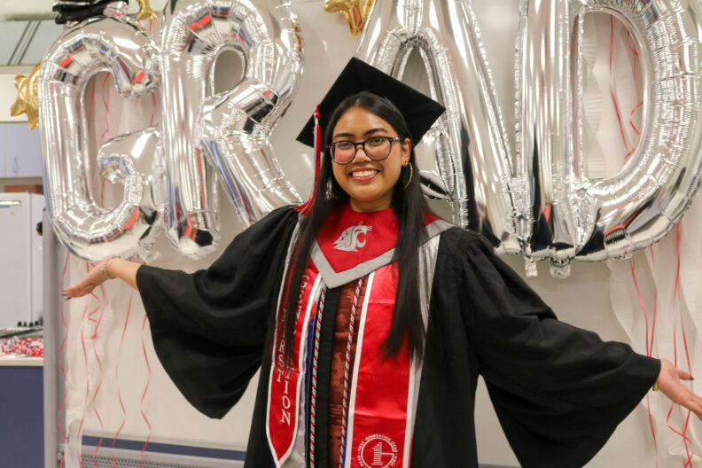 Sherine Ortiz raises up her arms. She stands in front of a decorate display.