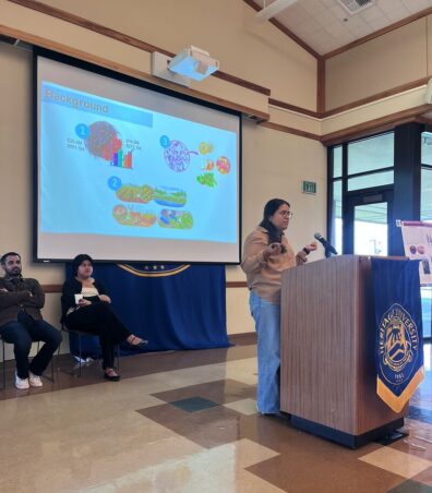 Miriam Ruiz stands at a podium talking. Her presentation is behind her.