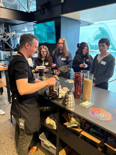 Food science students stand around a man pouring coffee from a french press into many different cups.