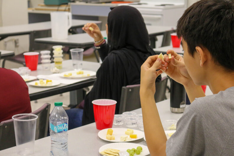A student breaks apart a square of cheese in his hand. Another student also examines a cube of cheese.