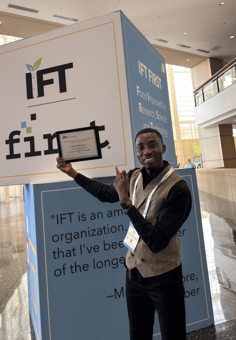 Paul holds up his award placard and points to a sign behind him that says IFT first.