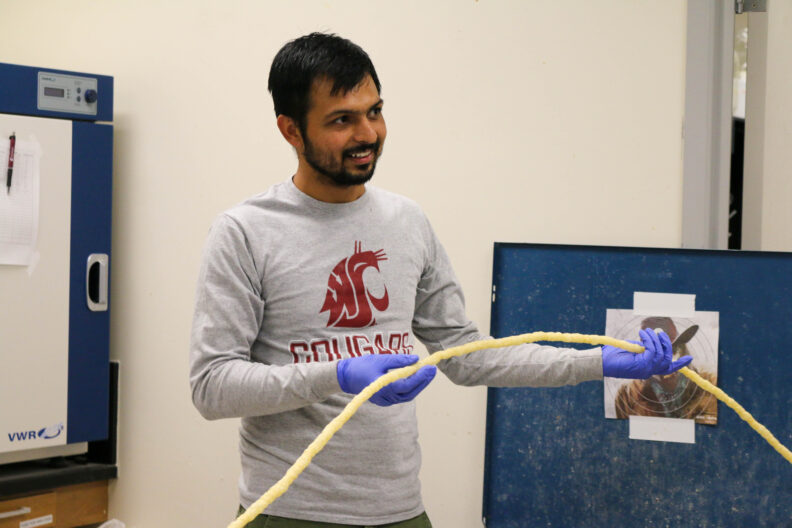 Aniket holds up a long strand of extruded material.
