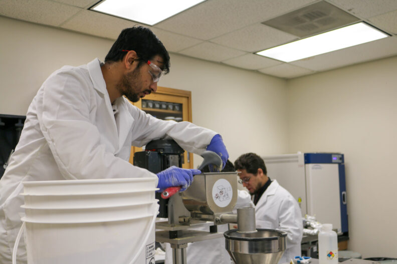 Aniket uses a ladle to pour powder into a receptacle in the extruder.