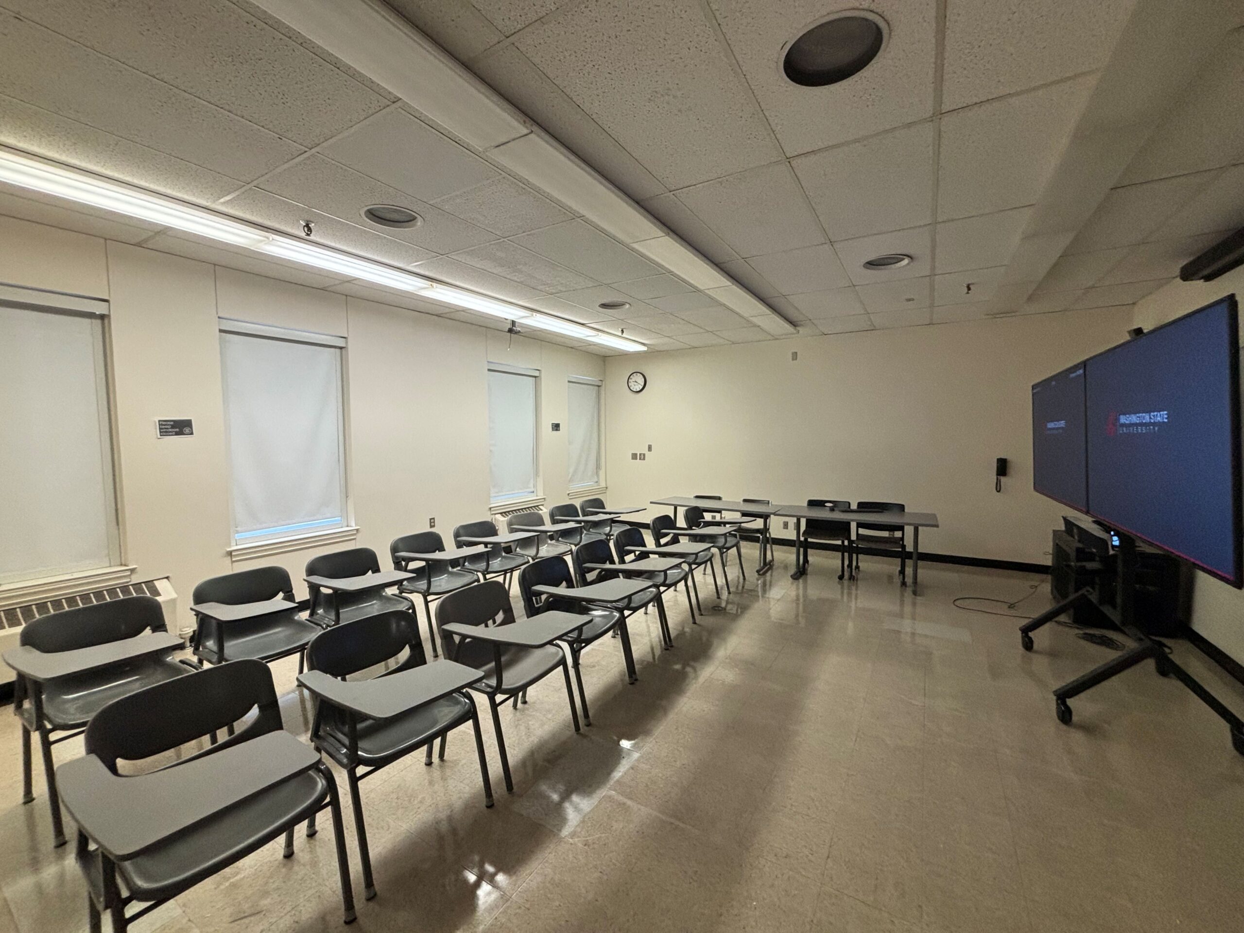 Looking out from the front corner of the room over the rows of tablet armchairs for student seating and toward the front of the room where two large screen displays are located.