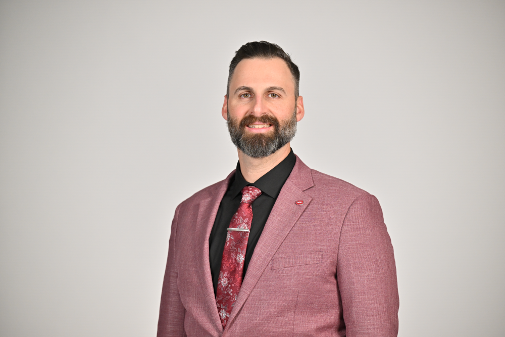 A professional headshot of Jon Haarlow wearing a crimson suit jacket and red tie.