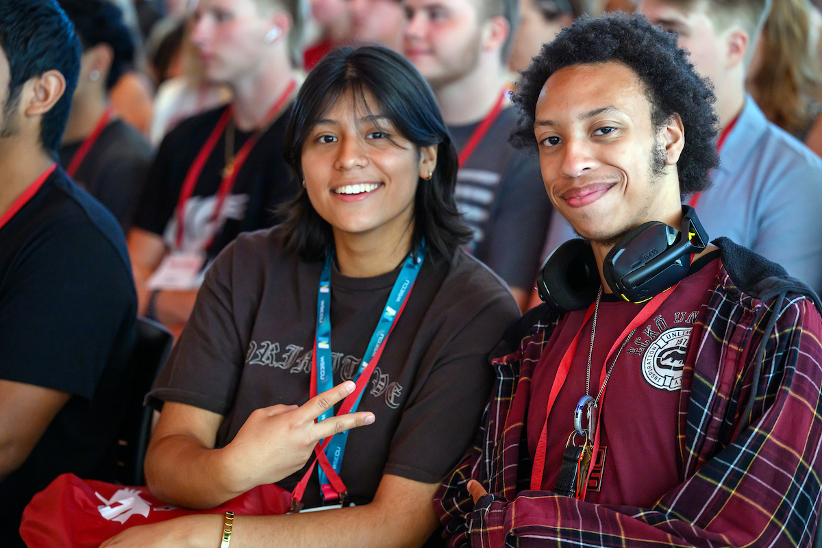 Two student at a campus event seated and smiling at the camera.