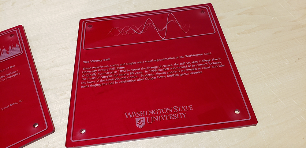 Photo: Wall plaque on The Victory Bell, showing a waveform and text: These waveforms, colors and shapes are a visual representation of the Washington State University Victory Bell chime. Originally purchased in 1892 to sound the change of classes, the bell sat atop College Hall in the heart of campus for almost 80 years. In 1998 the bell was moved to its current location, the lawn of the Lewis Alumni Centre. Students, alumni and fans are invited to come and take turns ringing the bell in celebration after cougar home football game victories.
