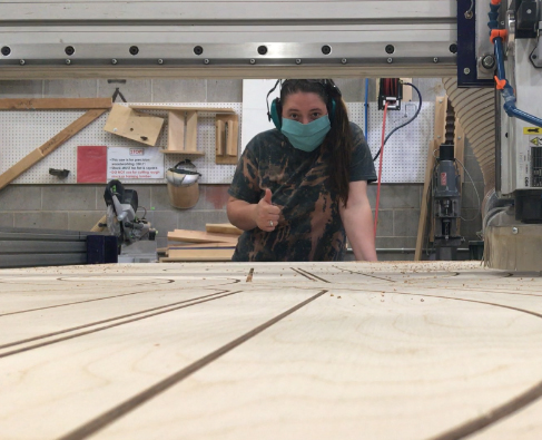 Photo: Student gives thumbs up behind CNC Milling and Cutting machine.