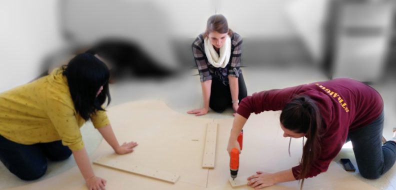 Photo: Three students work at fabricating early table prototype.