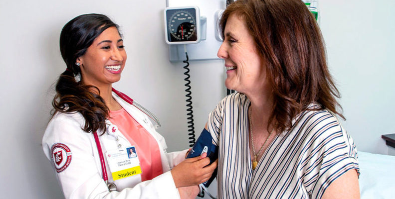 A WSU medical student is shown in an examination room, taking a patient's blood pressure.