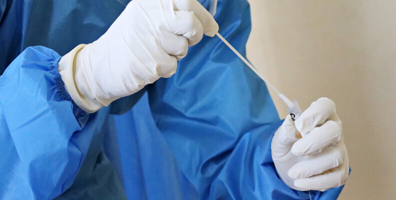 person in personal protective equipment is seen holding a swab