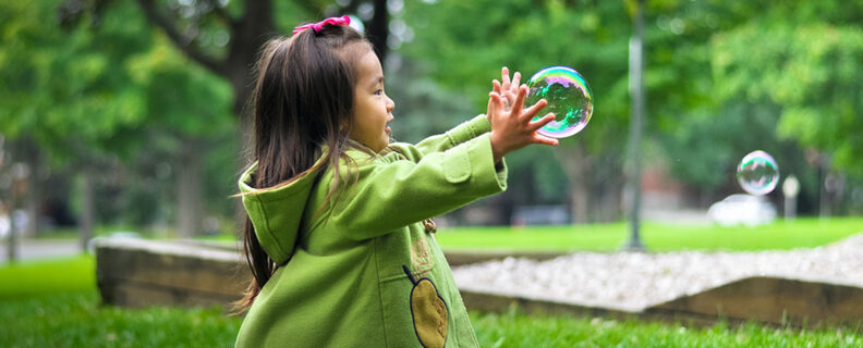 Little girl playing with soap bubbles in a city park