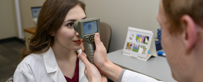A staff member in Georgina Lynch’s lab demonstrates the use of a handheld monocular pupillometer to measure the pupillary light reflex.