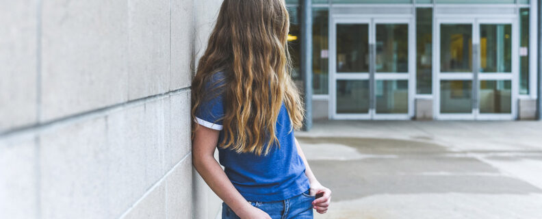Lone teenage girl standing in front of school