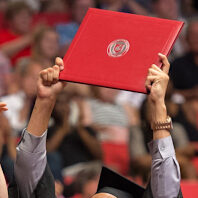 A WSU graduate holds up his diploma in celebration during a commencement ceremony.